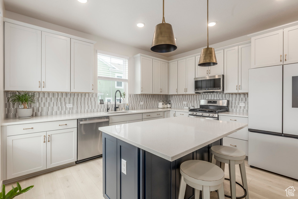 Kitchen featuring appliances with stainless steel finishes, a sink, light wood-type flooring, a kitchen breakfast bar, and recessed lighting