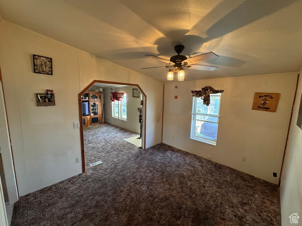 Empty room with carpet floors, arched walkways, and ceiling fan