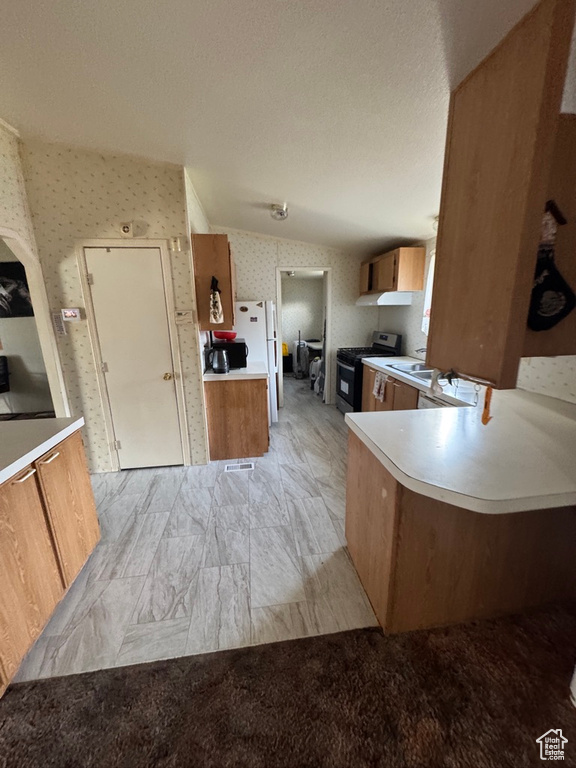 Kitchen featuring black gas stove, brown cabinetry, freestanding refrigerator, light countertops, and wallpapered walls