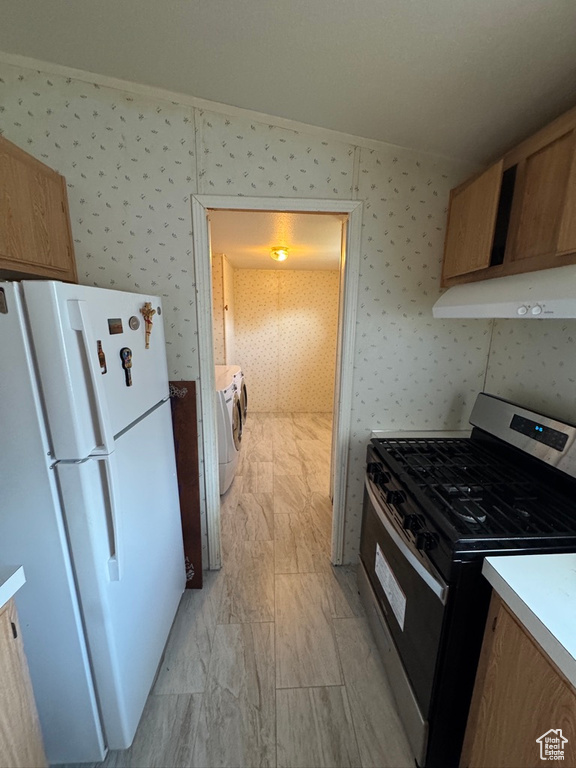 Kitchen with stainless steel range with gas stovetop, freestanding refrigerator, range hood, washing machine and clothes dryer, and wallpapered walls