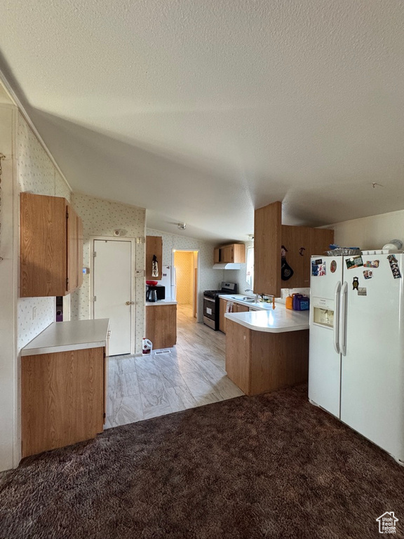 Kitchen with white fridge with ice dispenser, gas range, brown cabinetry, vaulted ceiling, and a textured ceiling
