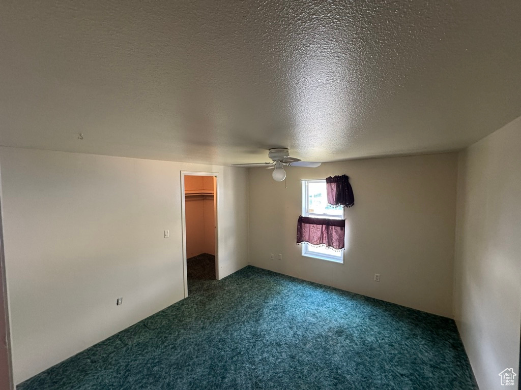 Unfurnished bedroom featuring dark colored carpet, a spacious closet, a textured ceiling, ceiling fan, and a closet
