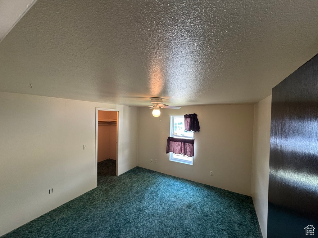 Unfurnished bedroom with carpet, a textured ceiling, a walk in closet, and ceiling fan