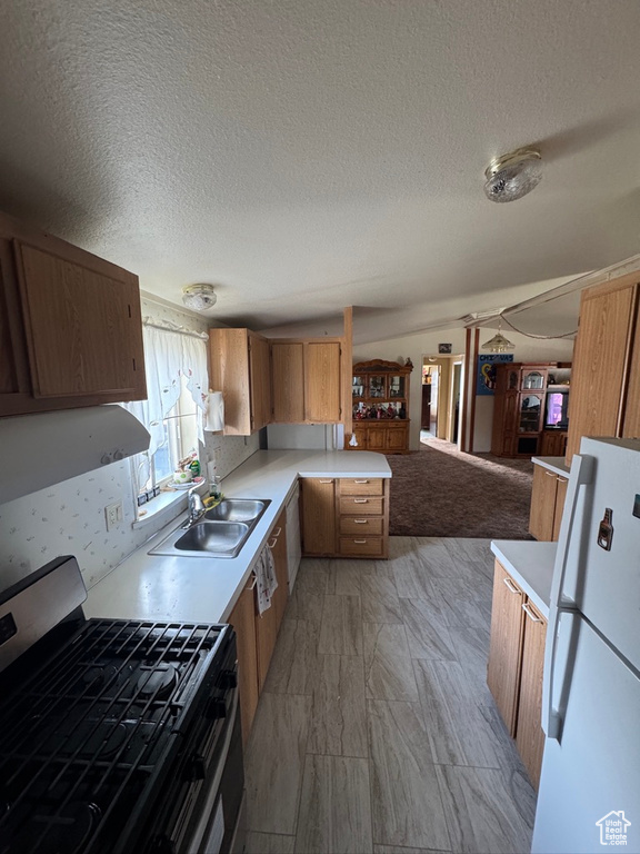 Kitchen with stainless steel gas range oven, freestanding refrigerator, a sink, light countertops, and a textured ceiling