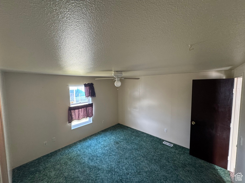 Unfurnished room with dark carpet, ceiling fan, and a textured ceiling