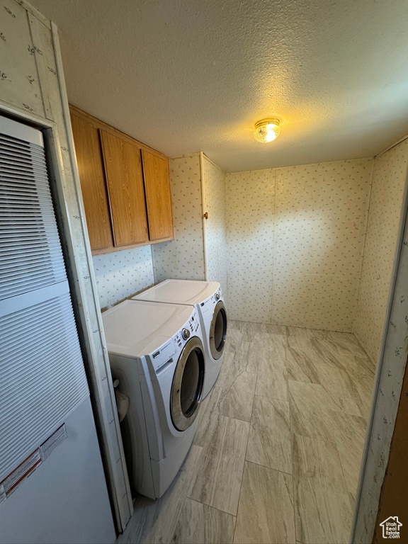 Washroom with cabinet space, washing machine and dryer, a textured ceiling, wallpapered walls, and a heating unit