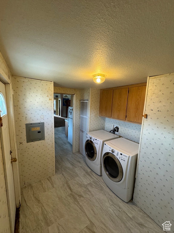 Washroom with cabinet space, wallpapered walls, washer and clothes dryer, and a textured ceiling