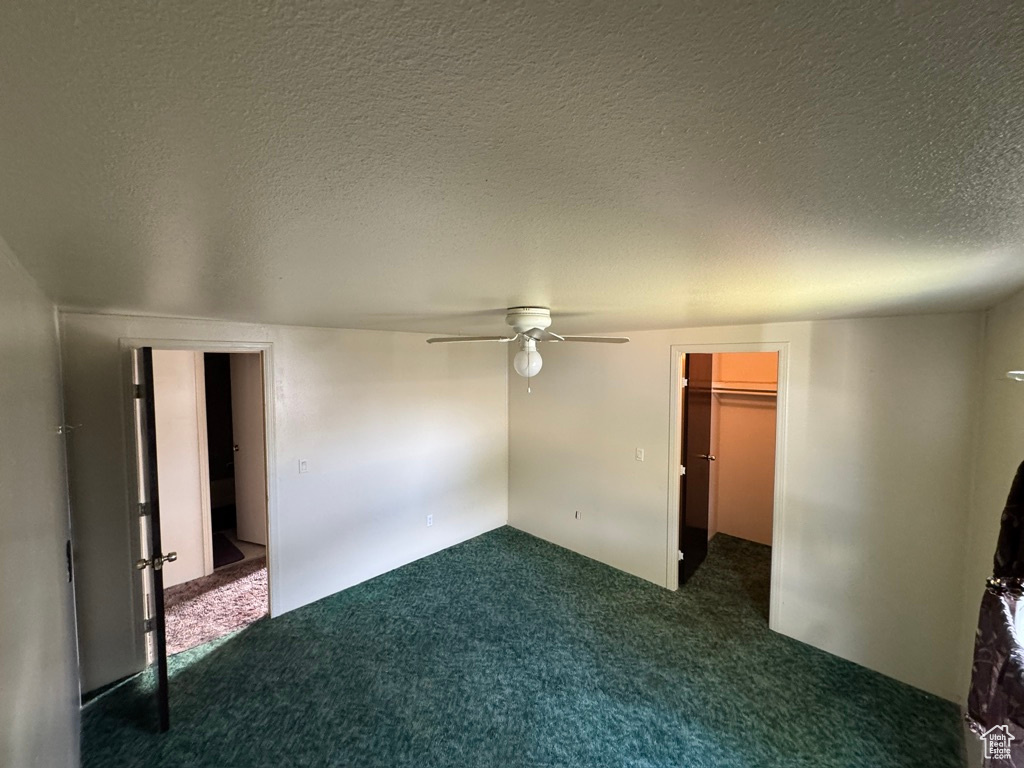 Unfurnished bedroom with carpet flooring, a textured ceiling, a spacious closet, and ceiling fan