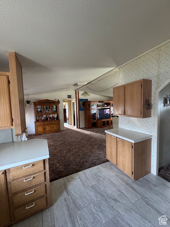 Kitchen with vaulted ceiling, open floor plan, a textured ceiling, brown cabinets, and light countertops