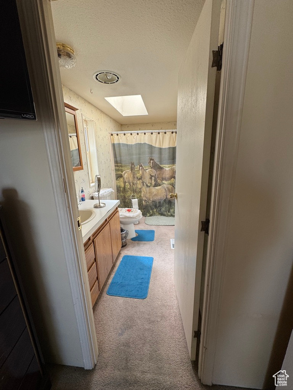 Full bathroom with a skylight, vanity, toilet, a textured ceiling, and curtained shower