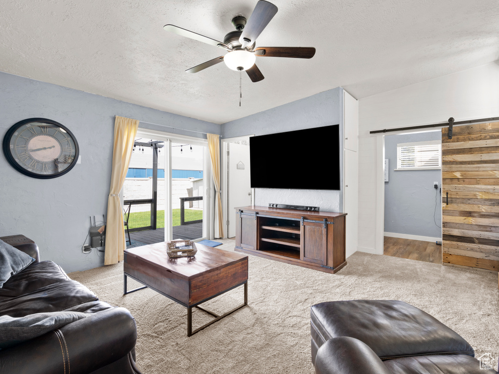 Living area with a ceiling fan, a barn door, light carpet, and a textured ceiling