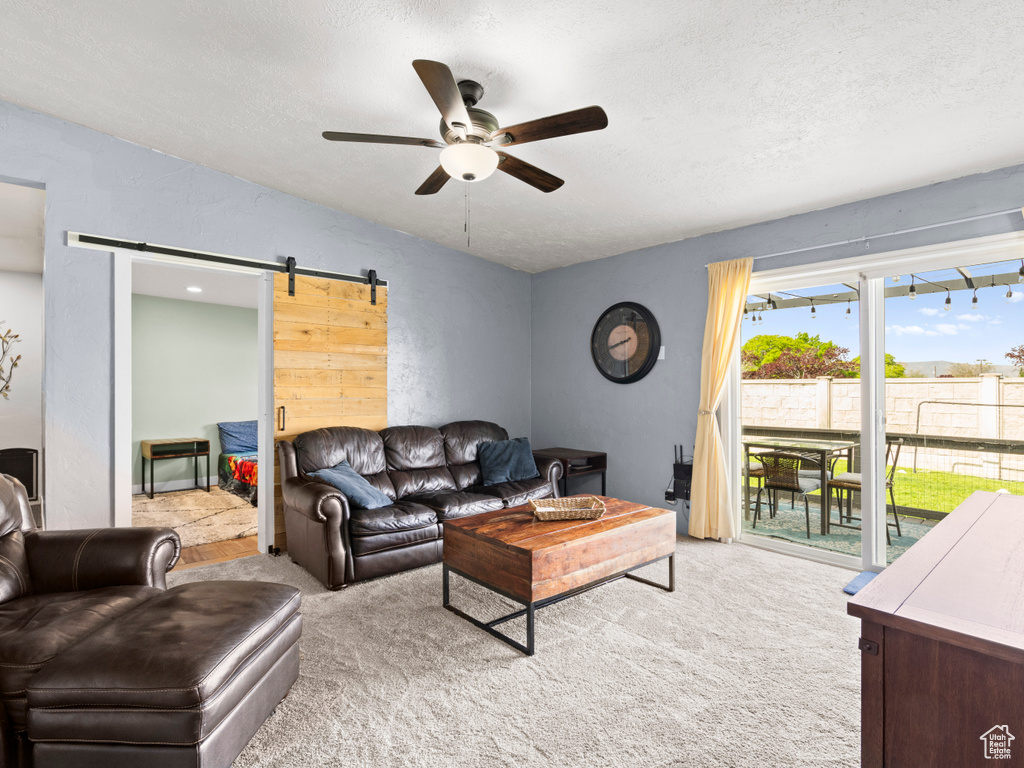 Carpeted living area with a ceiling fan, a barn door, and a textured ceiling