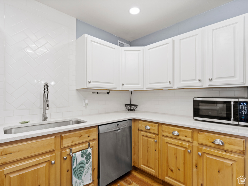 Kitchen with appliances with stainless steel finishes, a sink, backsplash, and light countertops