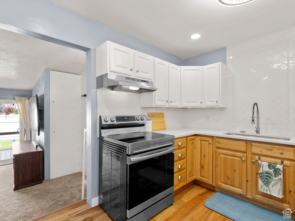 Kitchen featuring electric stove, under cabinet range hood, a sink, light wood-style floors, and backsplash