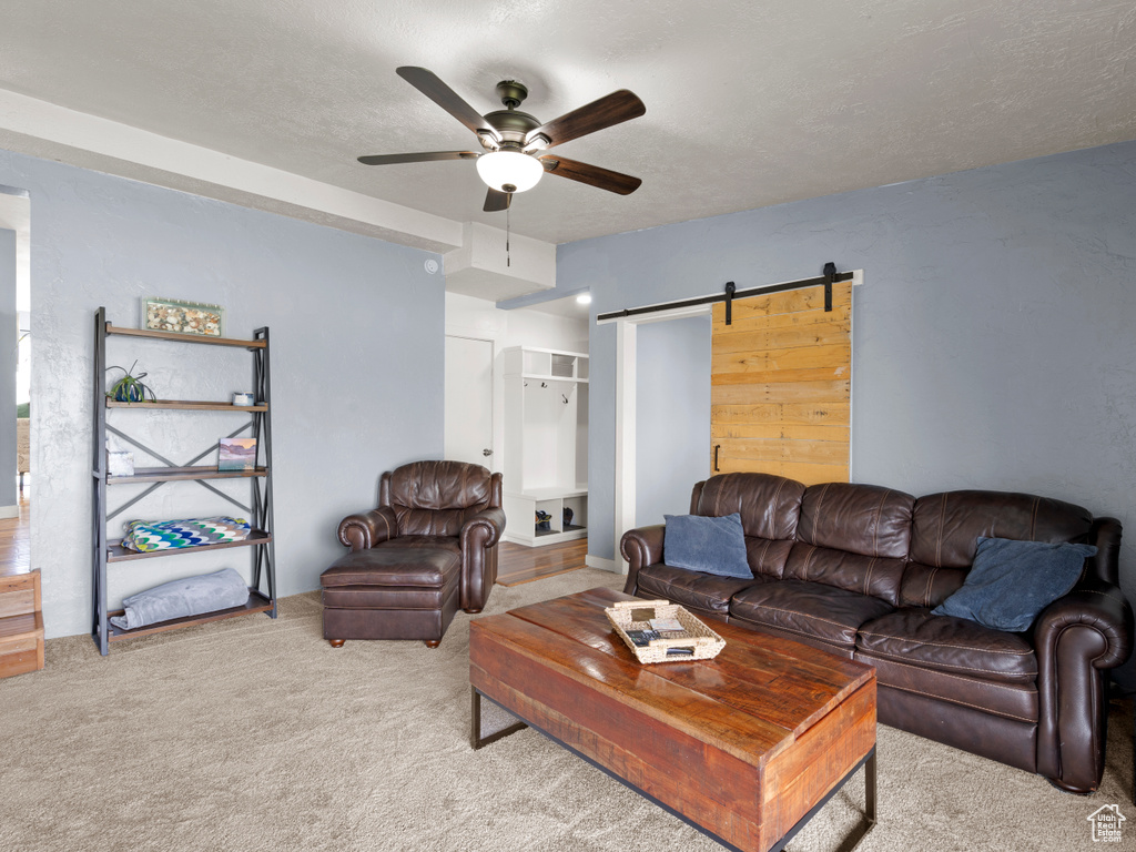 Carpeted living area with a barn door and a ceiling fan