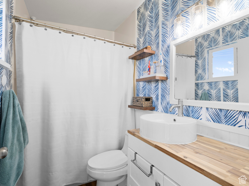 Bathroom featuring wallpapered walls, toilet, and vanity