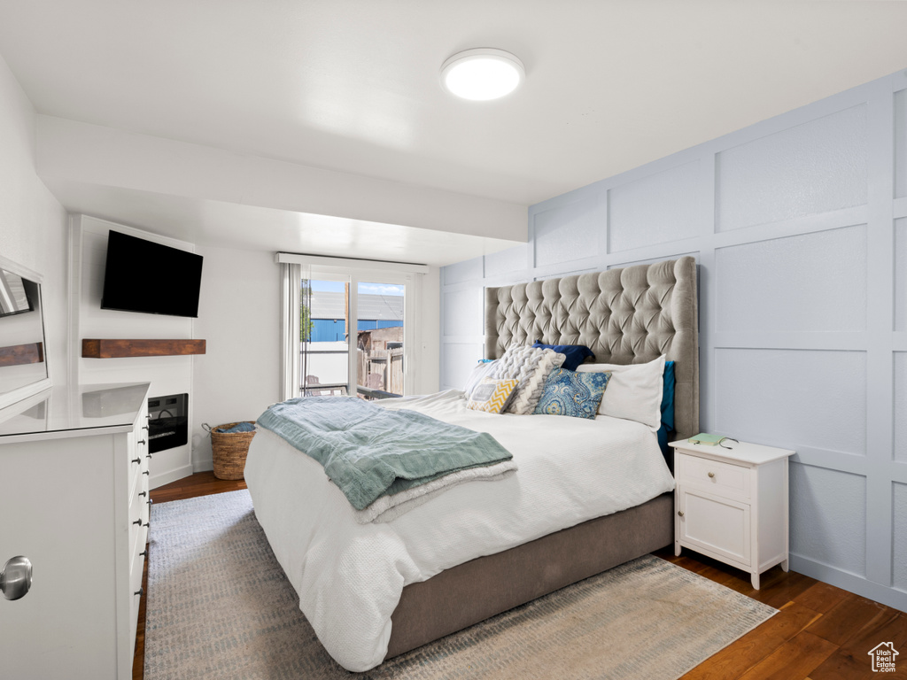 Bedroom with dark wood finished floors, a decorative wall, a glass covered fireplace, access to exterior, and baseboards