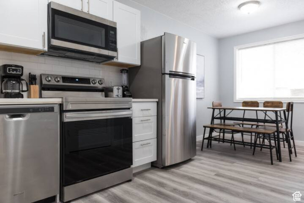 Kitchen with appliances with stainless steel finishes, white cabinets, backsplash, light wood-type flooring, and baseboards