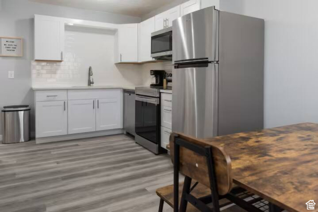 Kitchen featuring appliances with stainless steel finishes, a sink, light wood-style flooring, white cabinetry, and tasteful backsplash