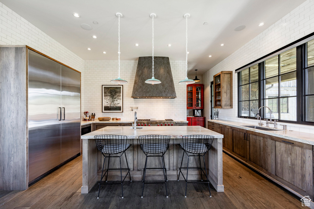Kitchen with a sink, stainless steel built in refrigerator, premium range hood, a kitchen bar, and a kitchen island with sink