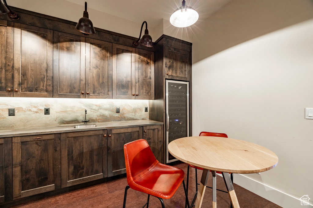 Kitchen featuring backsplash, dark brown cabinetry, a sink, beverage cooler, and light countertops
