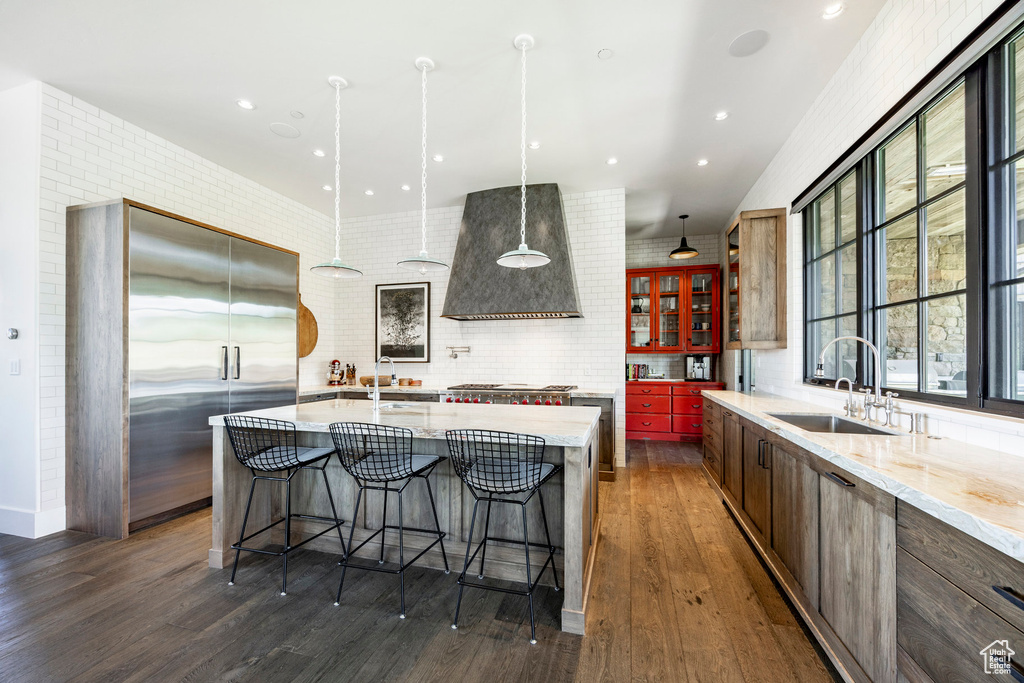 Kitchen with a sink, wall chimney range hood, appliances with stainless steel finishes, dark wood-style flooring, and a breakfast bar