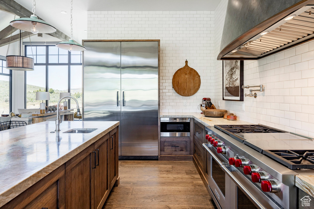 Kitchen featuring premium appliances, a sink, extractor fan, tasteful backsplash, and wood finished floors