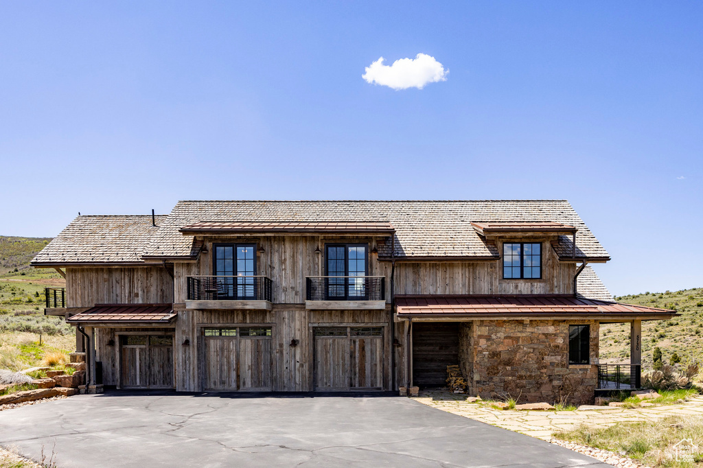 View of front of home featuring a balcony, driveway, a garage, a standing seam roof, and metal roof