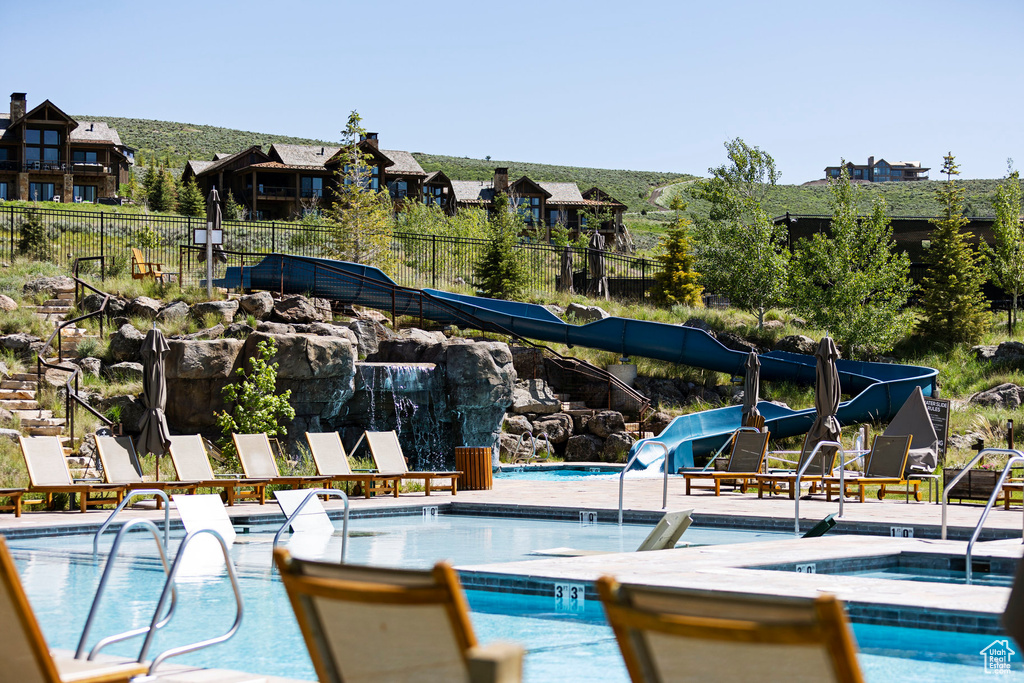 Community pool with a hot tub, a water slide, and fence