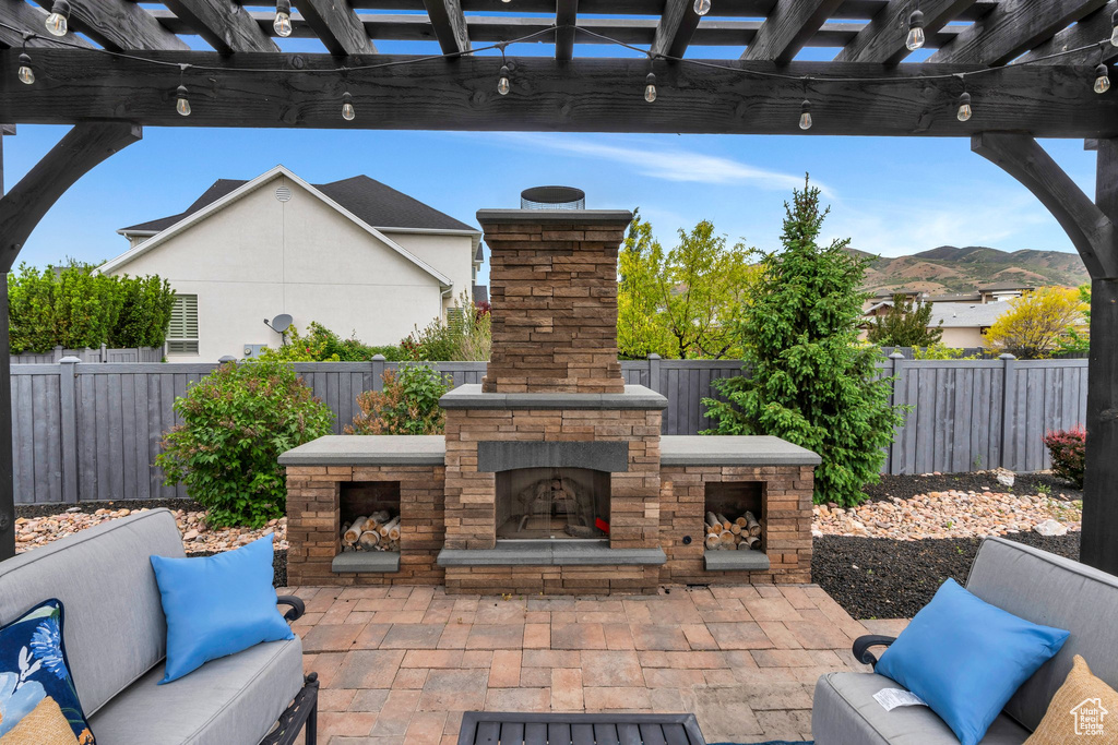 View of patio with an outdoor stone fireplace, a fenced backyard, a mountain view, and a pergola