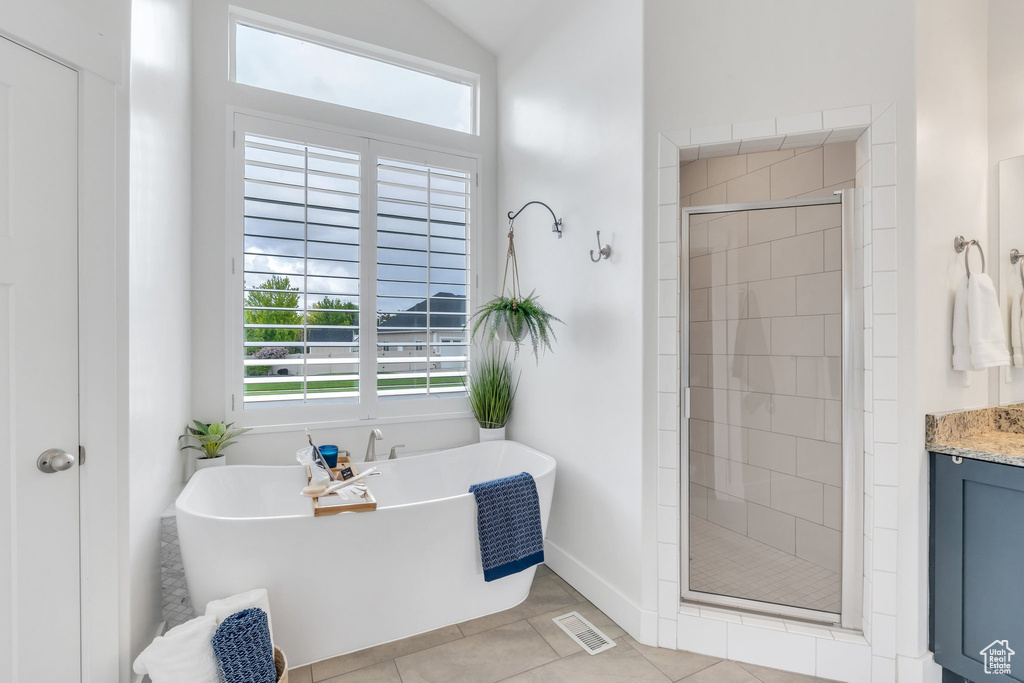 Bathroom featuring a stall shower, tile patterned floors, a freestanding tub, vanity, and baseboards