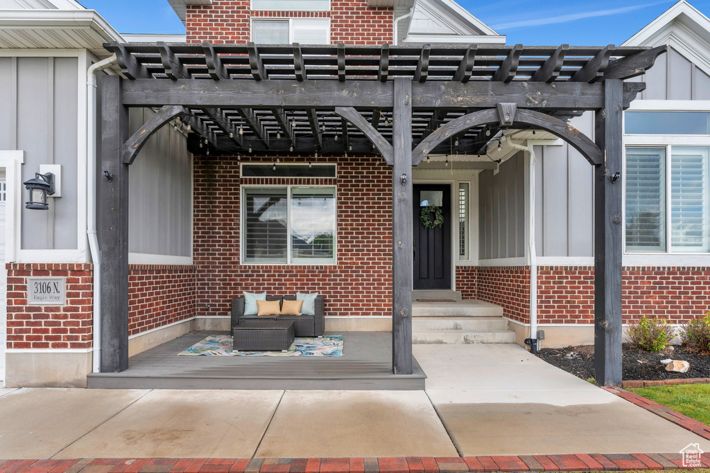 Property entrance with brick siding, a pergola, and board and batten siding