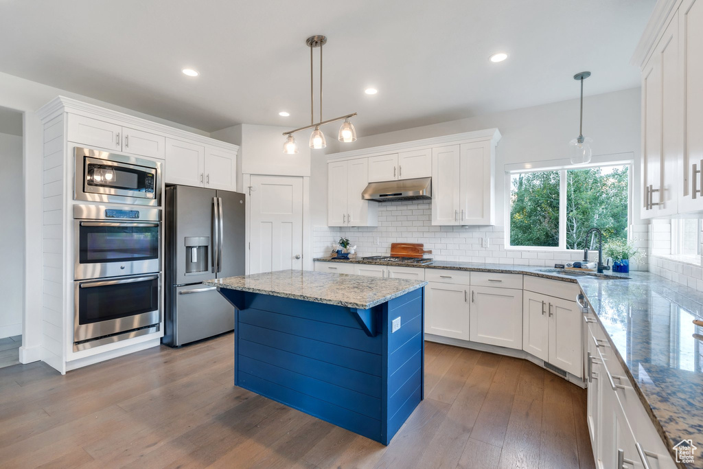 Kitchen with appliances with stainless steel finishes, under cabinet range hood, a sink, white cabinetry, and decorative backsplash