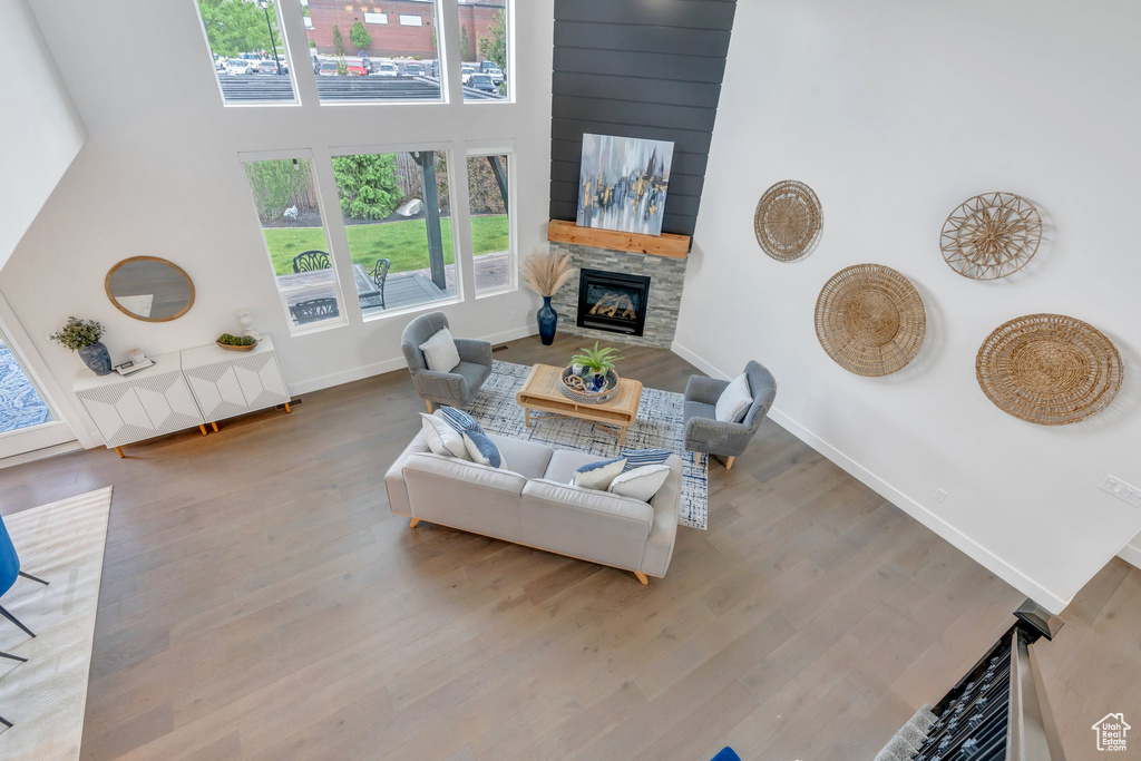 Living area featuring a stone fireplace, wood finished floors, baseboards, and a high ceiling