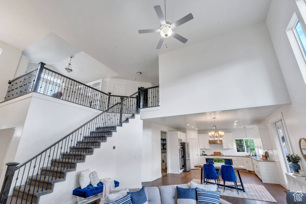 Living room featuring a chandelier, a high ceiling, a ceiling fan, dark wood-style floors, and stairway