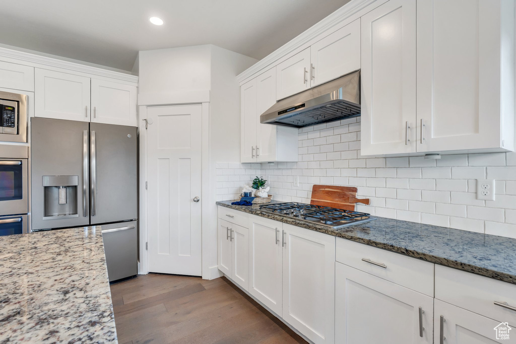 Kitchen featuring stainless steel appliances, under cabinet range hood, white cabinetry, wood finished floors, and recessed lighting
