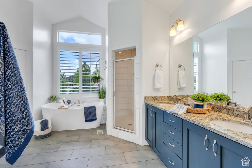 Full bathroom featuring a shower stall, a freestanding bath, double vanity, tile patterned flooring, and high vaulted ceiling