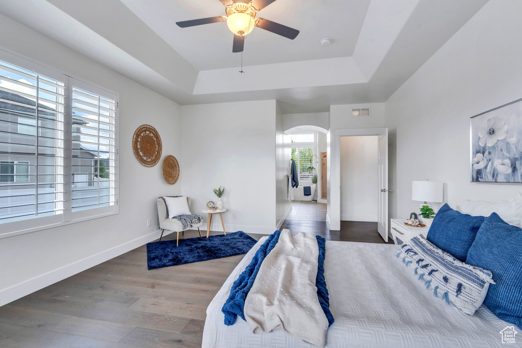 Bedroom featuring arched walkways, a tray ceiling, wood finished floors, and baseboards
