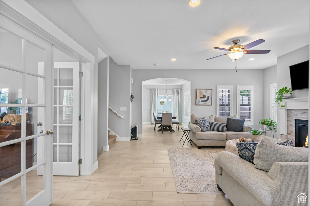 Living area with arched walkways, stairs, a glass covered fireplace, ceiling fan, and recessed lighting