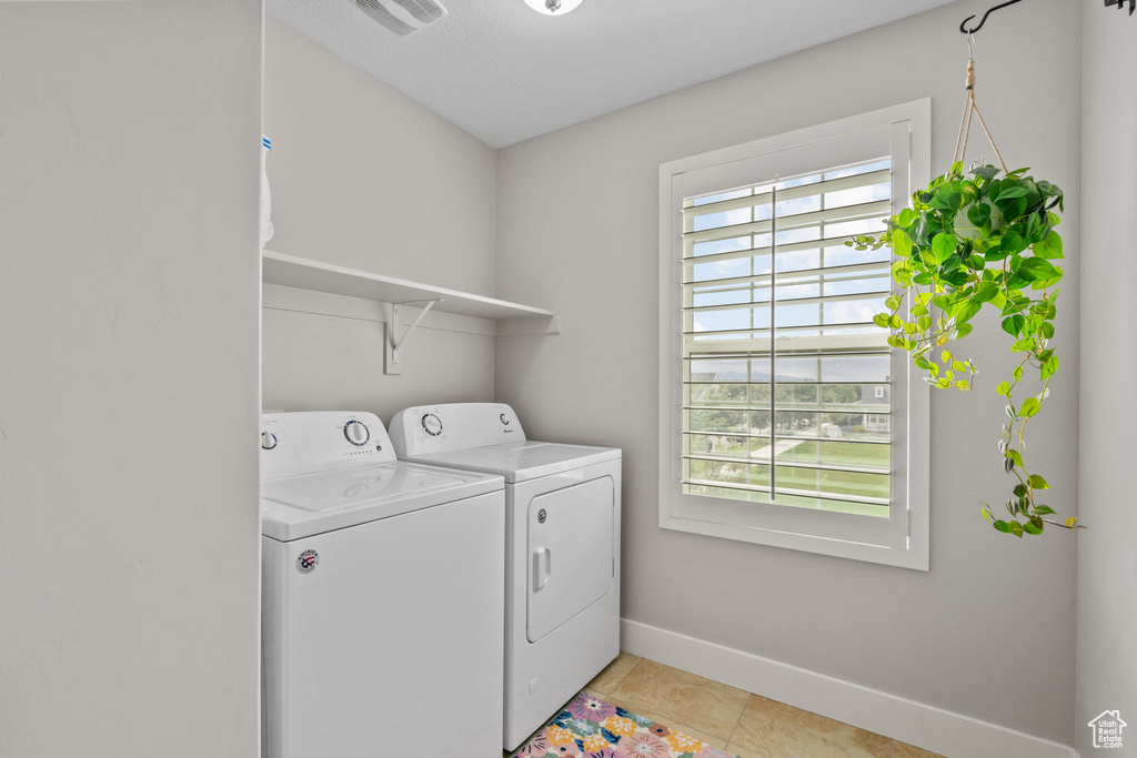Clothes washing area featuring washer and clothes dryer, baseboards, and light tile patterned flooring