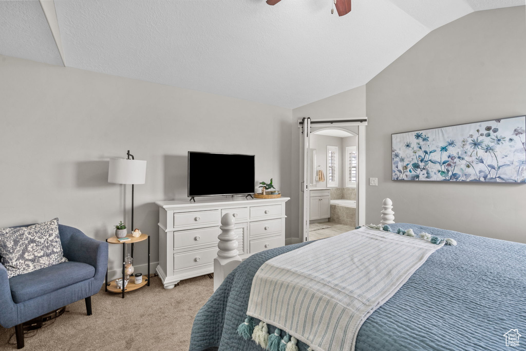 Bedroom featuring vaulted ceiling, light carpet, arched walkways, ensuite bath, and ceiling fan