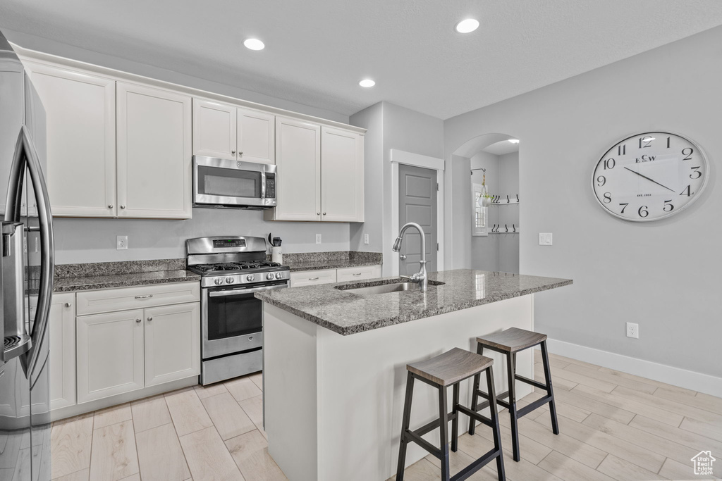 Kitchen featuring appliances with stainless steel finishes, a sink, arched walkways, dark stone countertops, and white cabinetry