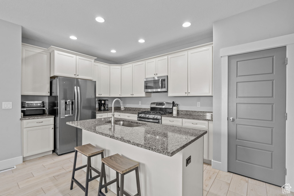 Kitchen featuring stainless steel appliances, a sink, recessed lighting, dark stone countertops, and white cabinetry