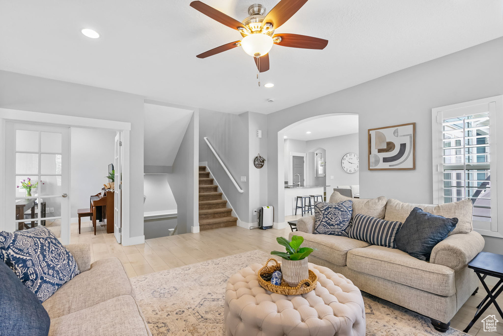 Living area with stairs, ceiling fan, arched walkways, light wood-style floors, and recessed lighting
