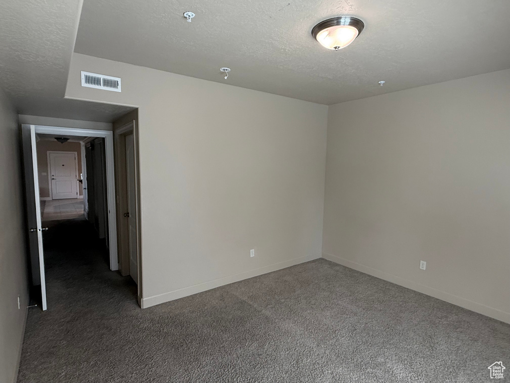 Carpeted spare room with a textured ceiling, baseboards, and a pendent fire sprinkler