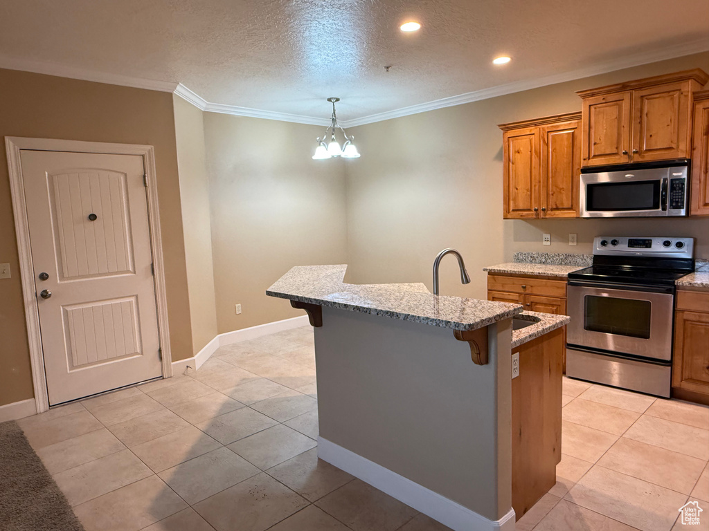 Kitchen with appliances with stainless steel finishes, a breakfast bar, brown cabinetry, a chandelier, and light stone counters