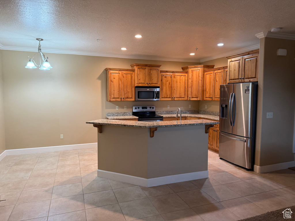 Kitchen featuring stainless steel appliances, light stone countertops, a kitchen bar, brown cabinets, and ornamental molding