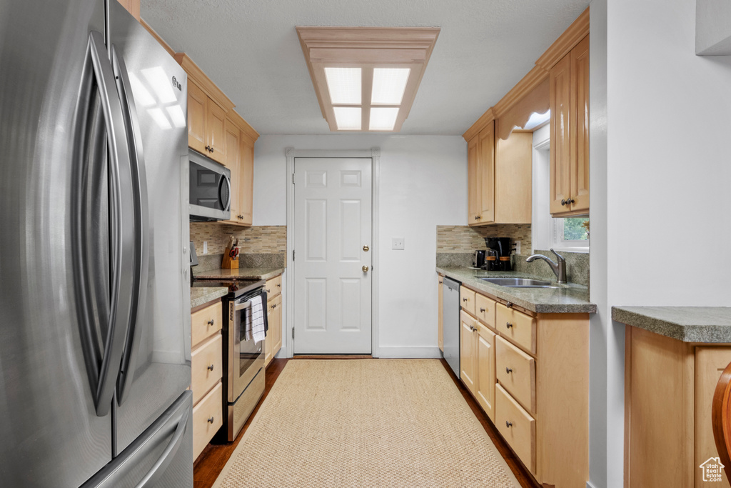 Kitchen with stainless steel appliances, a sink, tasteful backsplash, and light brown cabinetry