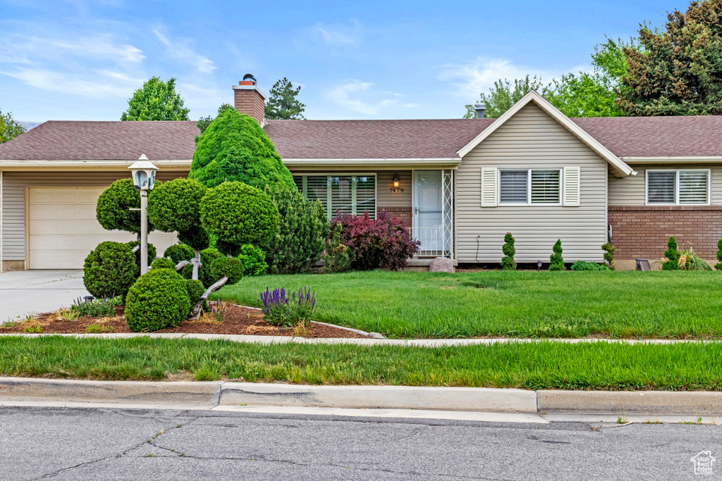 Ranch-style home with an attached garage, a chimney, brick siding, concrete driveway, and a front yard
