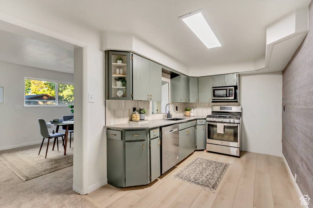 Kitchen with appliances with stainless steel finishes, a sink, light countertops, green cabinets, and light wood-style floors